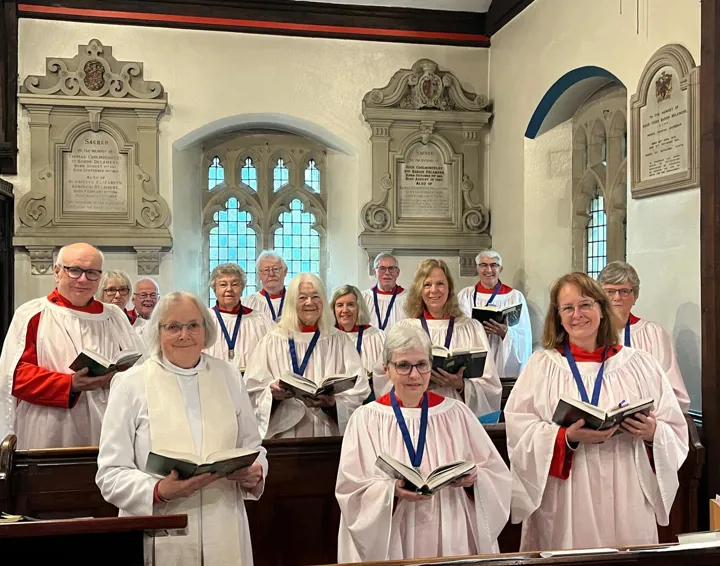 Church choir in red cassocks and white surplices holding hymn books standing in choir stalls