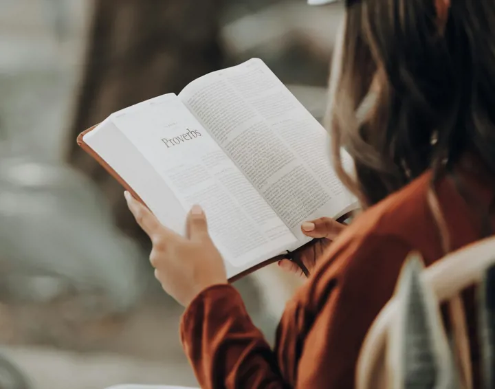 This is a photo looking over a woman's shoulder to the open bible that she is reading.