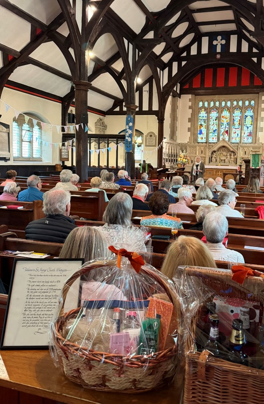 People sat in the pews in the church with raffle prize hampers in the foreground