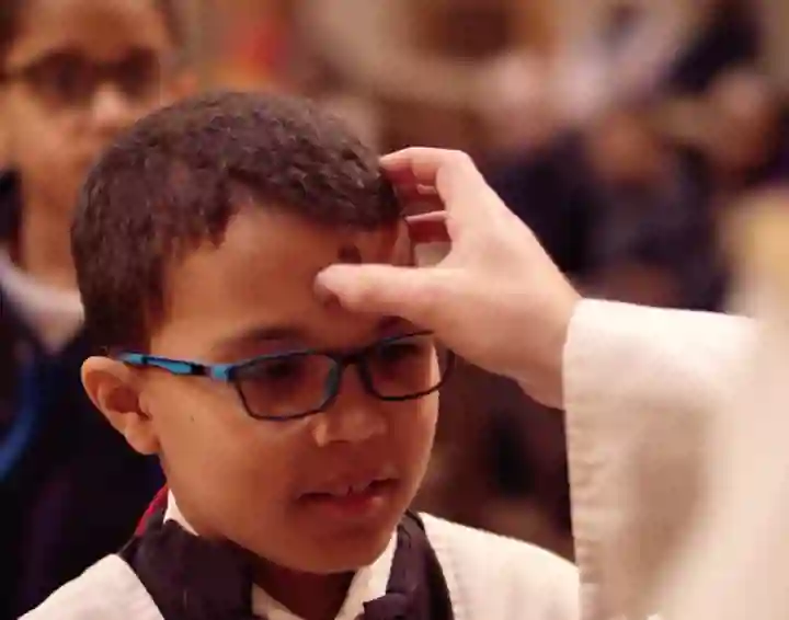 Boy having an ash cross made on his forehead.