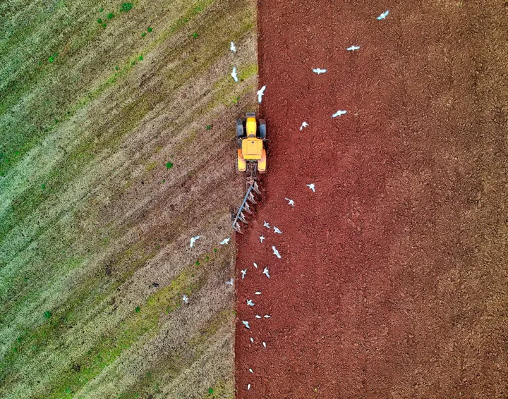 Aerial view of a yellow tractor ploughing a field