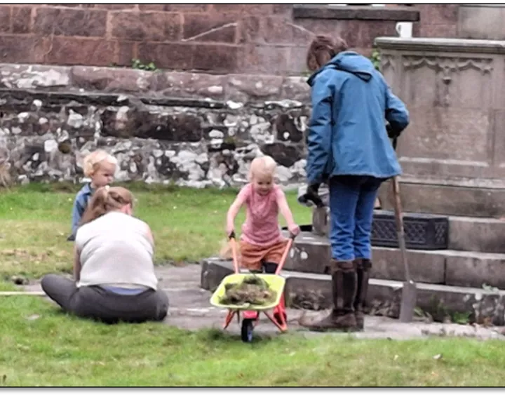 A lady and several children tidying the graveyard next to the cenotaph