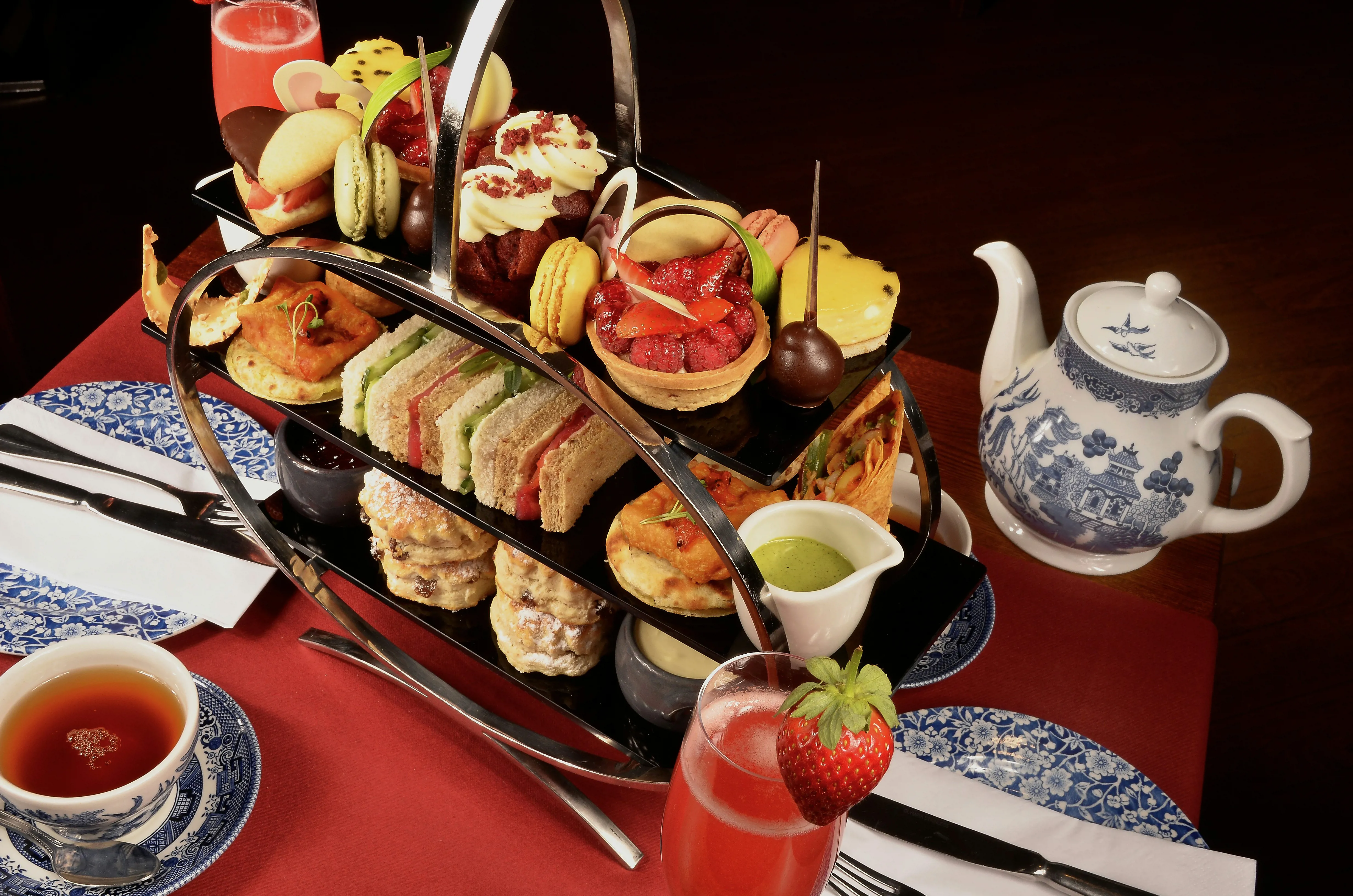 Afternoon tea on a tiered carrier with sandwiches and cakes and a pot of tea beside it.