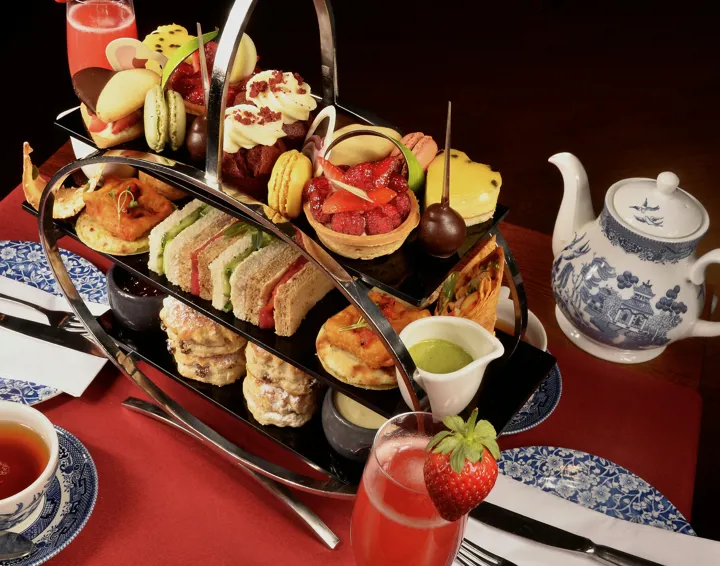 Afternoon tea on a tiered carrier with sandwiches and cakes and a pot of tea beside it.