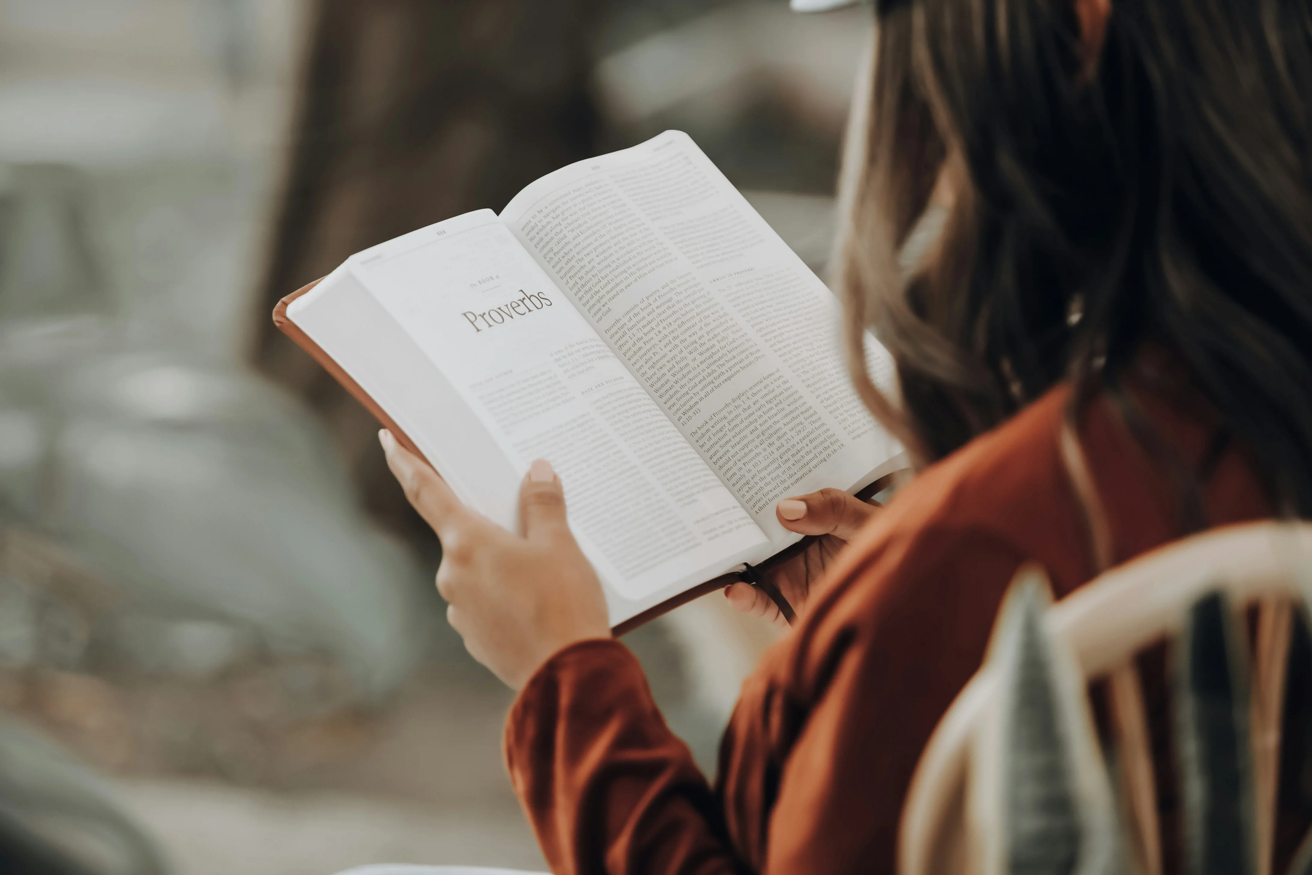 This is a photo looking over a woman's shoulder to the open bible that she is reading.