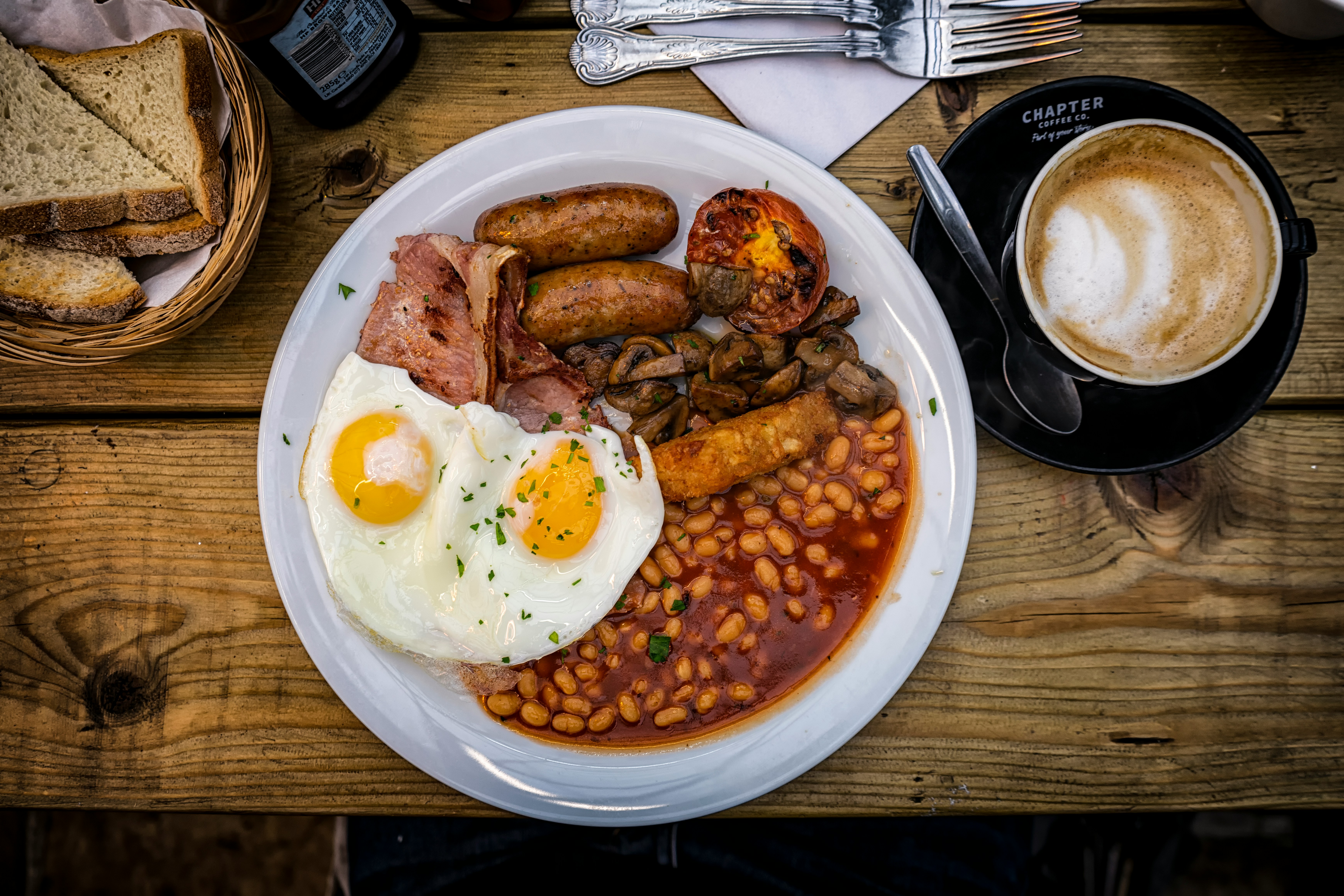 Cooked English breakfast on a plate with a cup of coffee on the side