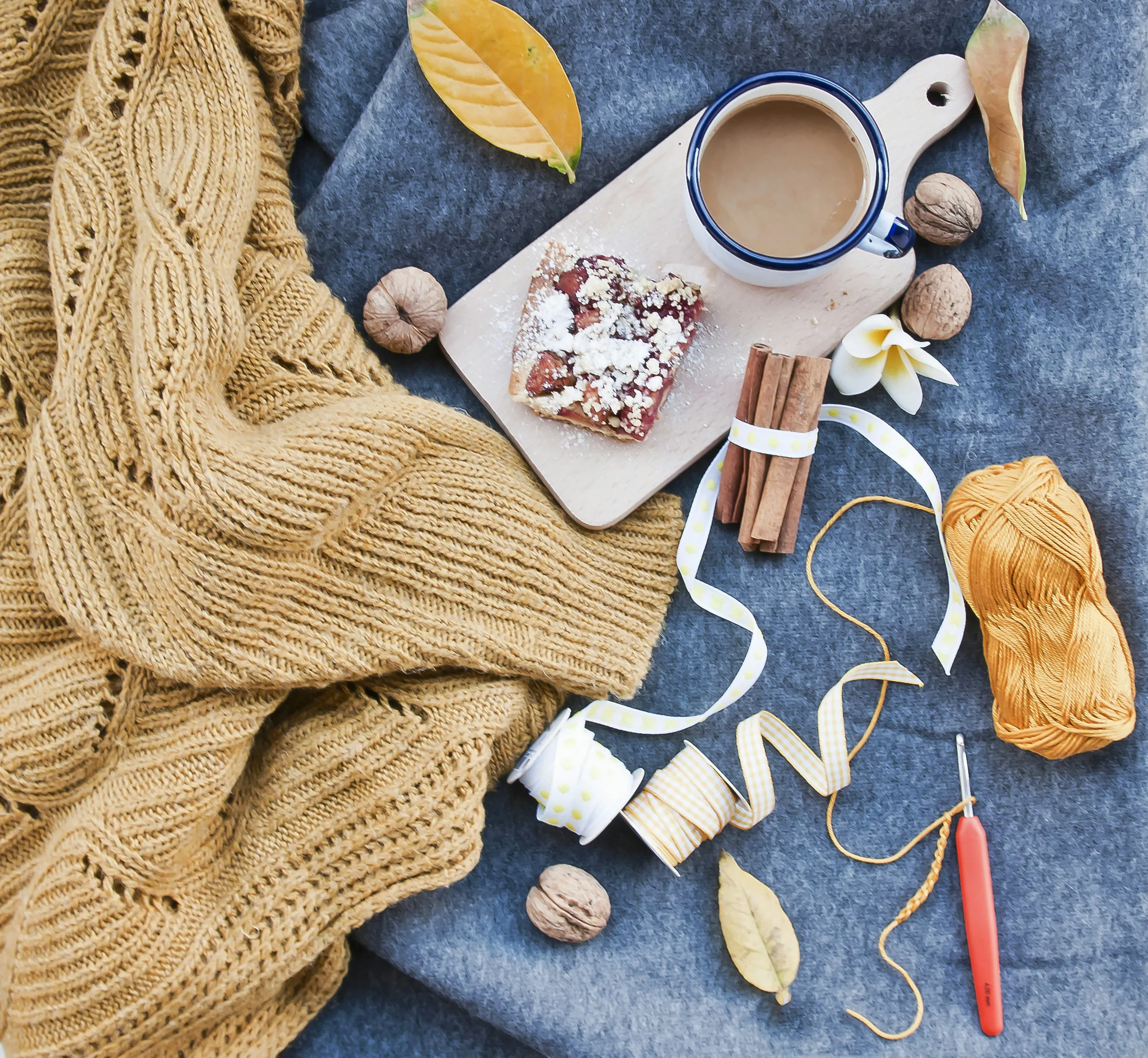 A table with a jumper, wool, crochet needle and a mug of tea and cake