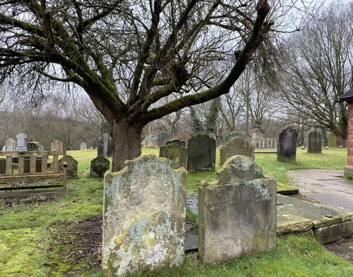 Photo across St Mary's graveyard with two old gravestones in the foreground and a bare tree behind.