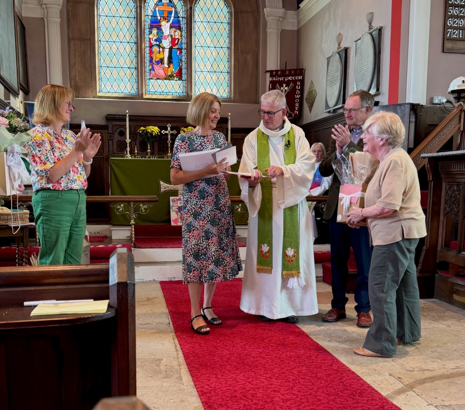The Vicar and his wife in the chancel receiving retirement gifts from 3 church wardens who are clapping